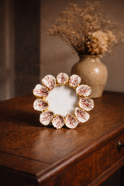 Decorative circular object with floral design on a wooden surface, with a vase of dried flowers in the background.