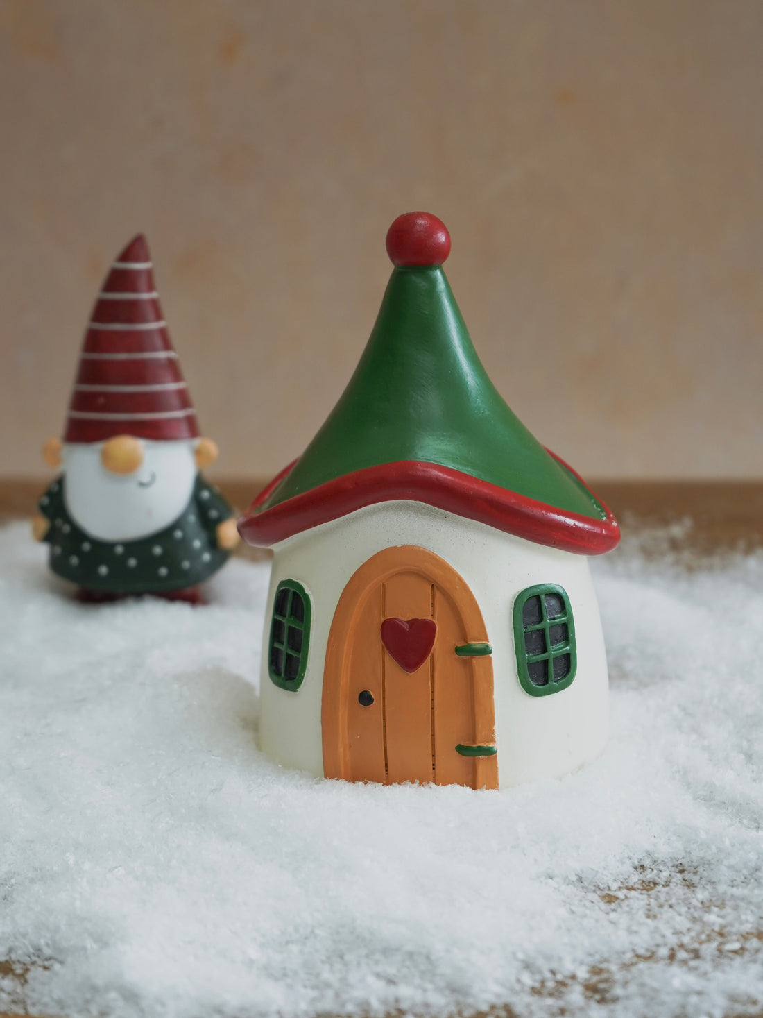 Small fairy house with a gnome in the background on a snowy surface