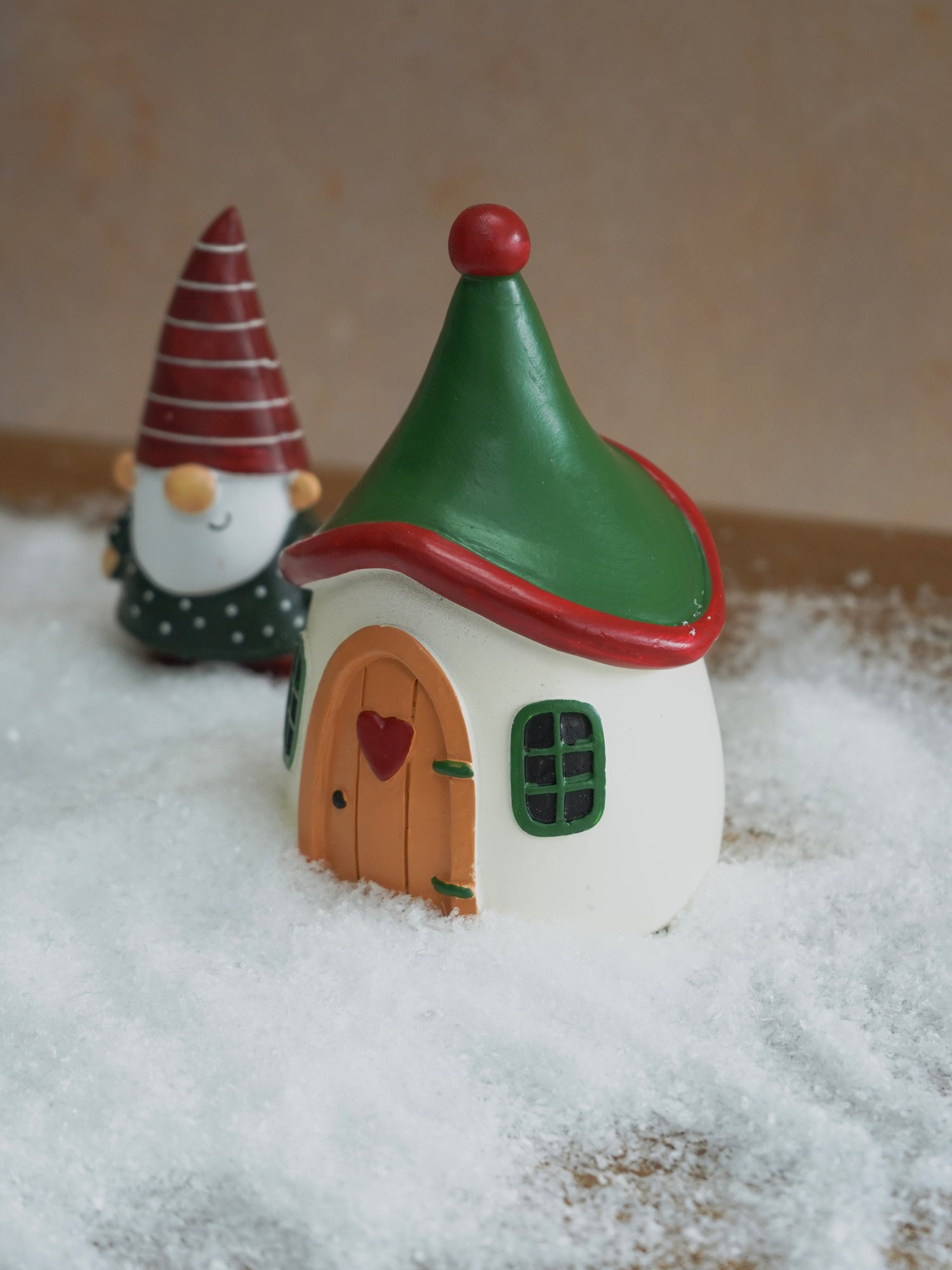 Small fairy house with a green roof and red trim, placed on a snowy surface.
