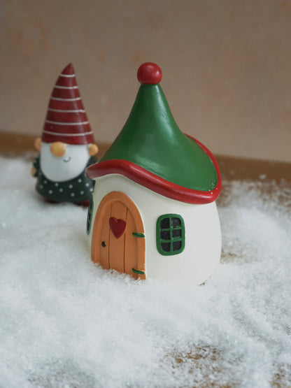 Small fairy house with a green roof and red trim, placed on a snowy surface.