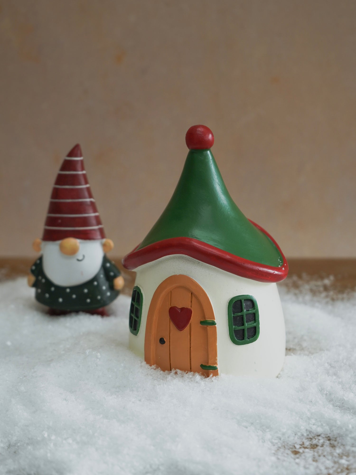 Fairy house with a green roof and small gnome figurine on a snowy surface