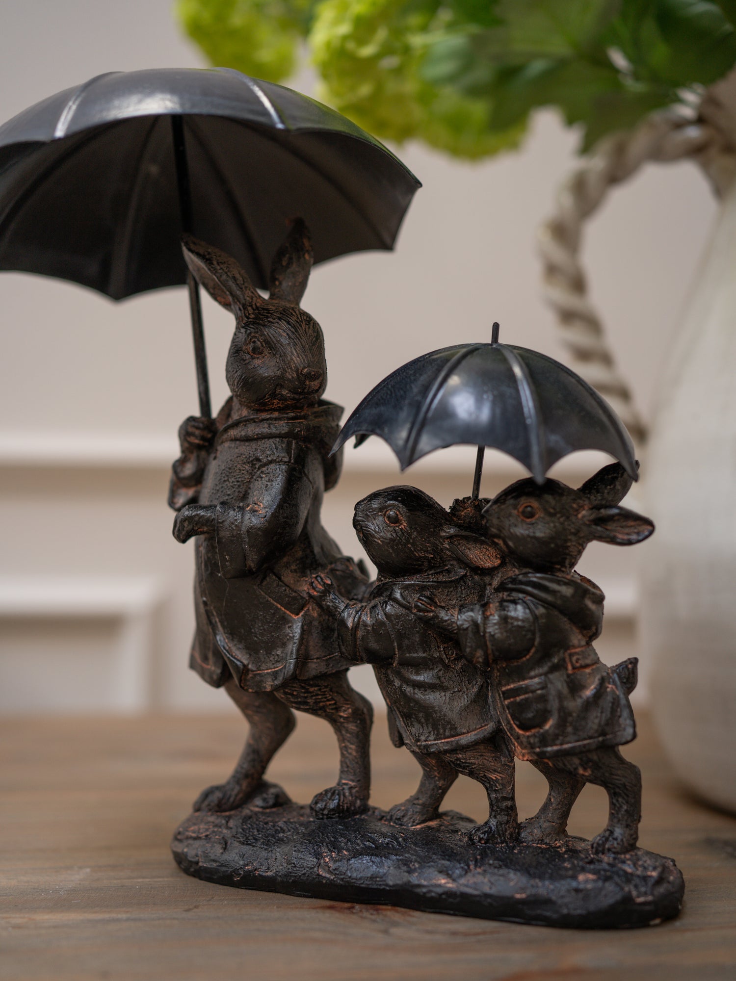 Bronze sculpture of three rabbits with umbrellas on a wooden surface