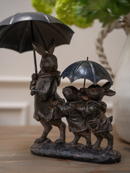 Bronze sculpture of three rabbits with umbrellas on a wooden surface