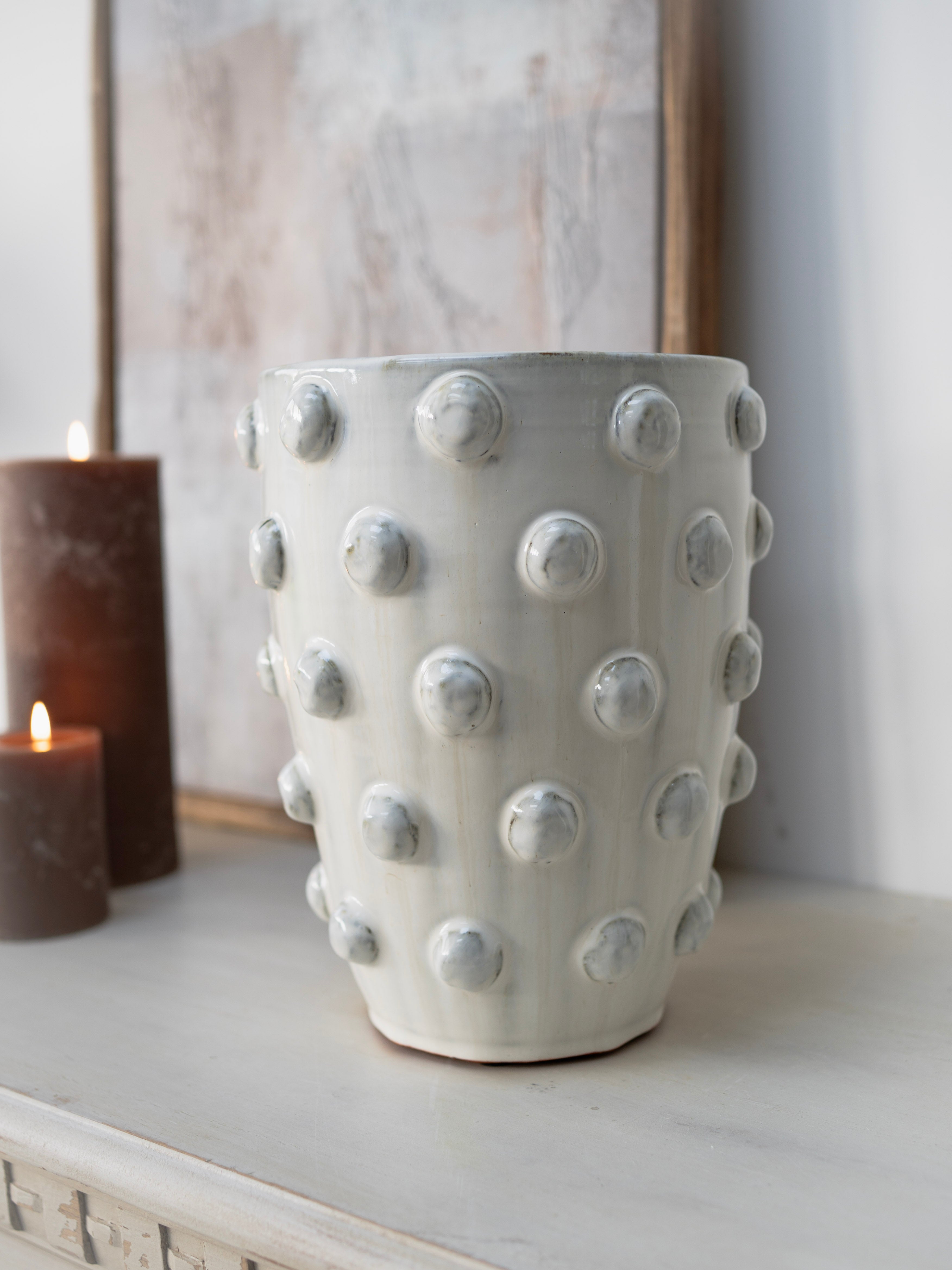 White textured vase on a surface with a candle and framed picture in the background