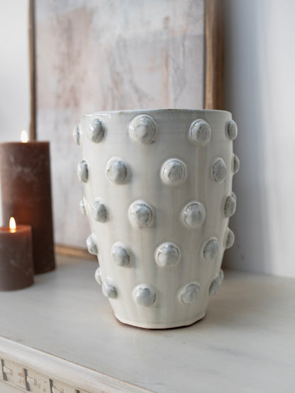White textured vase on a surface with a candle and framed picture in the background