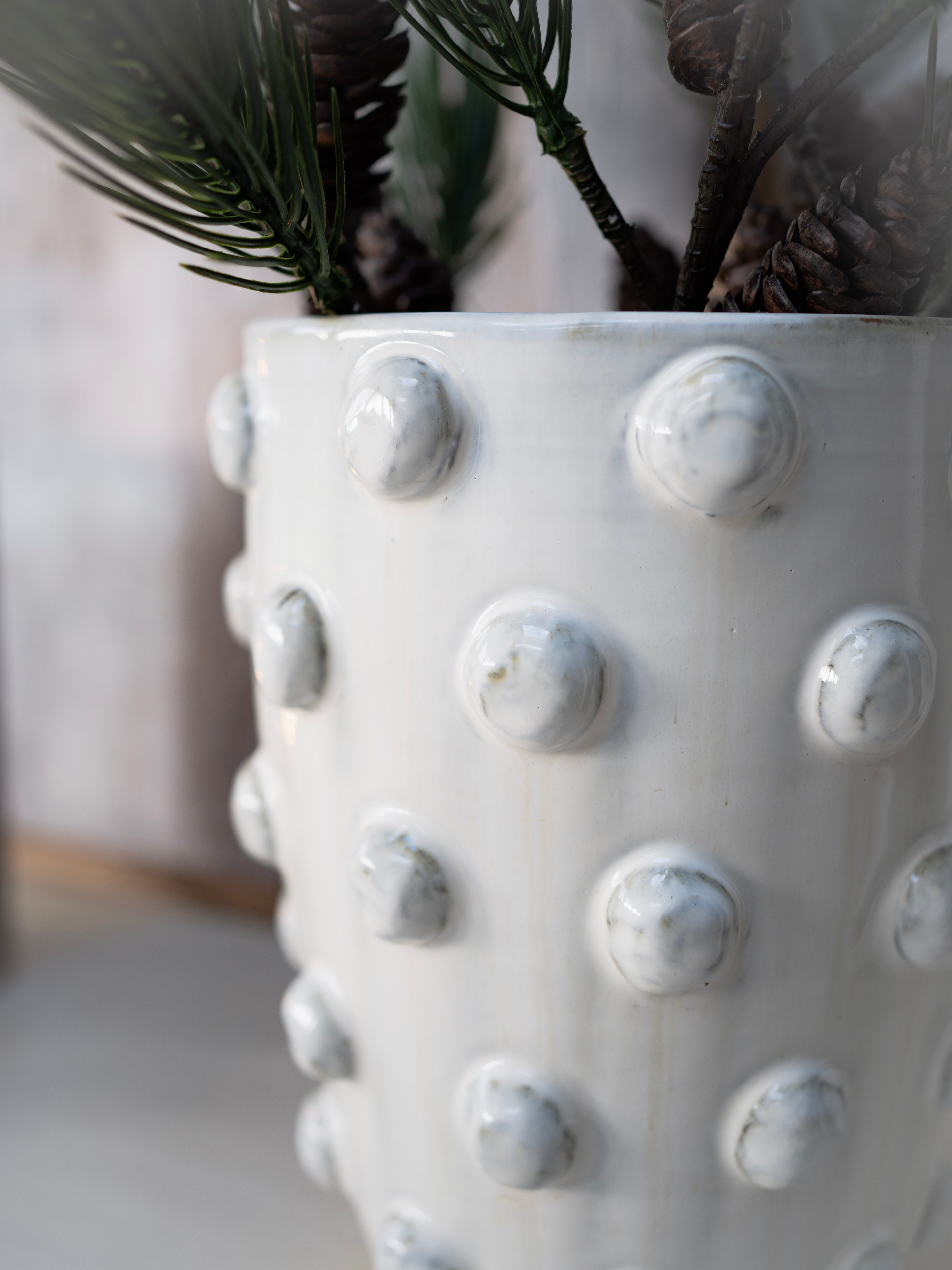 White textured vase with decorative knobs holding greenery.