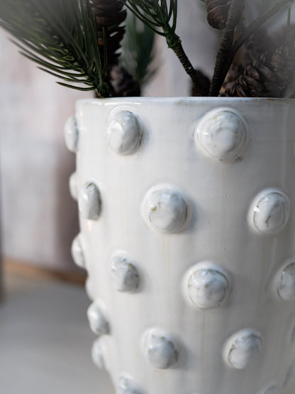 White textured vase with decorative knobs holding greenery.