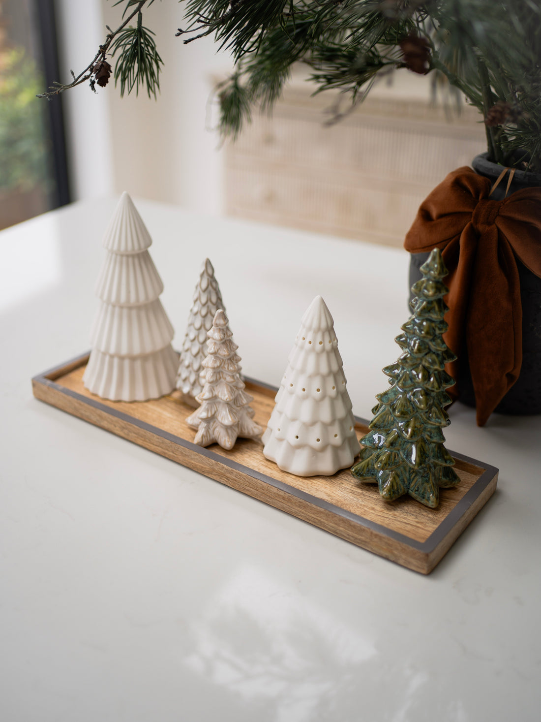 Decorative ceramic Christmas trees on a wooden tray with a neutral background