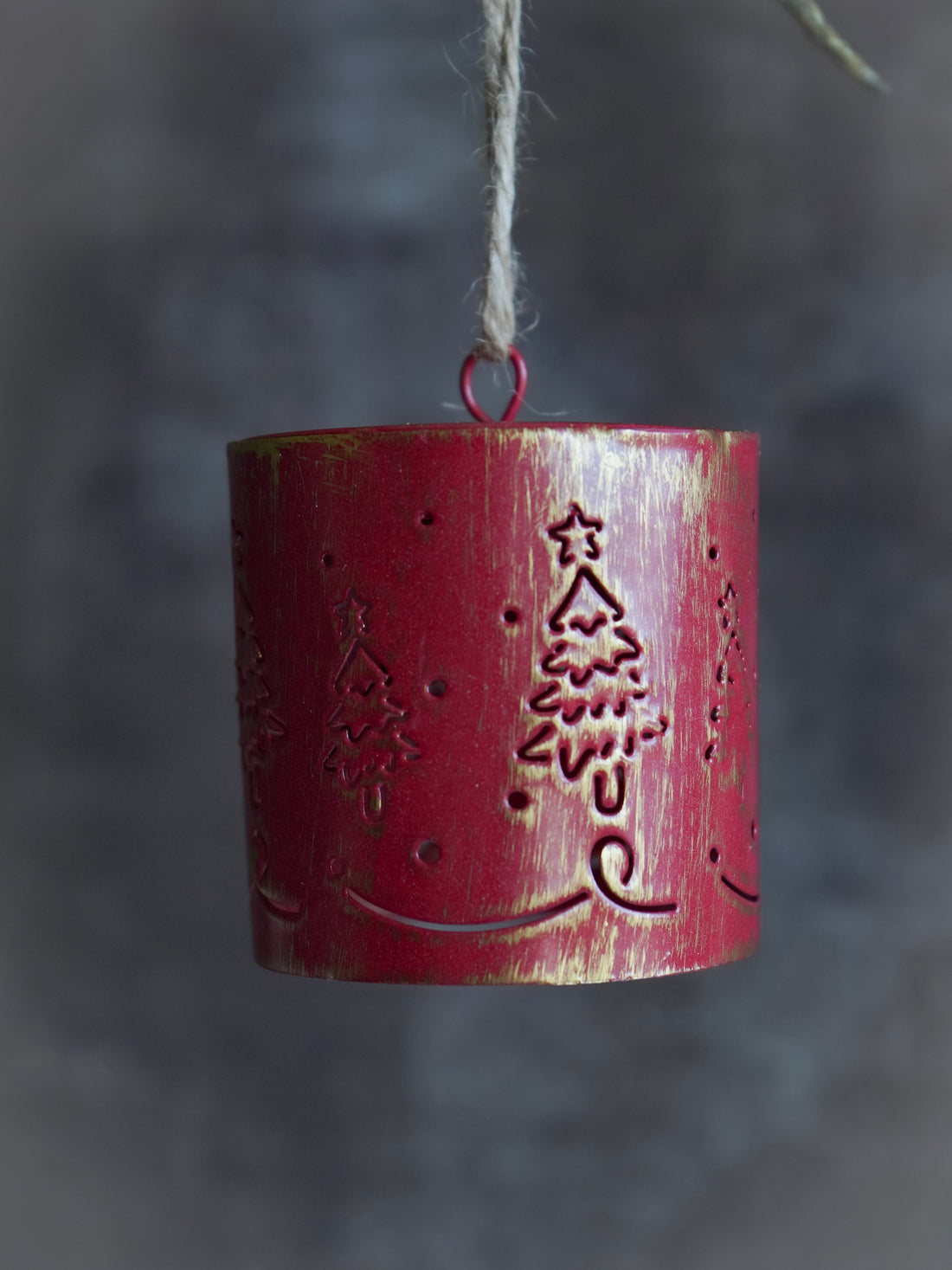 Red cylindrical hanging bell ornament with tree design on a dark background