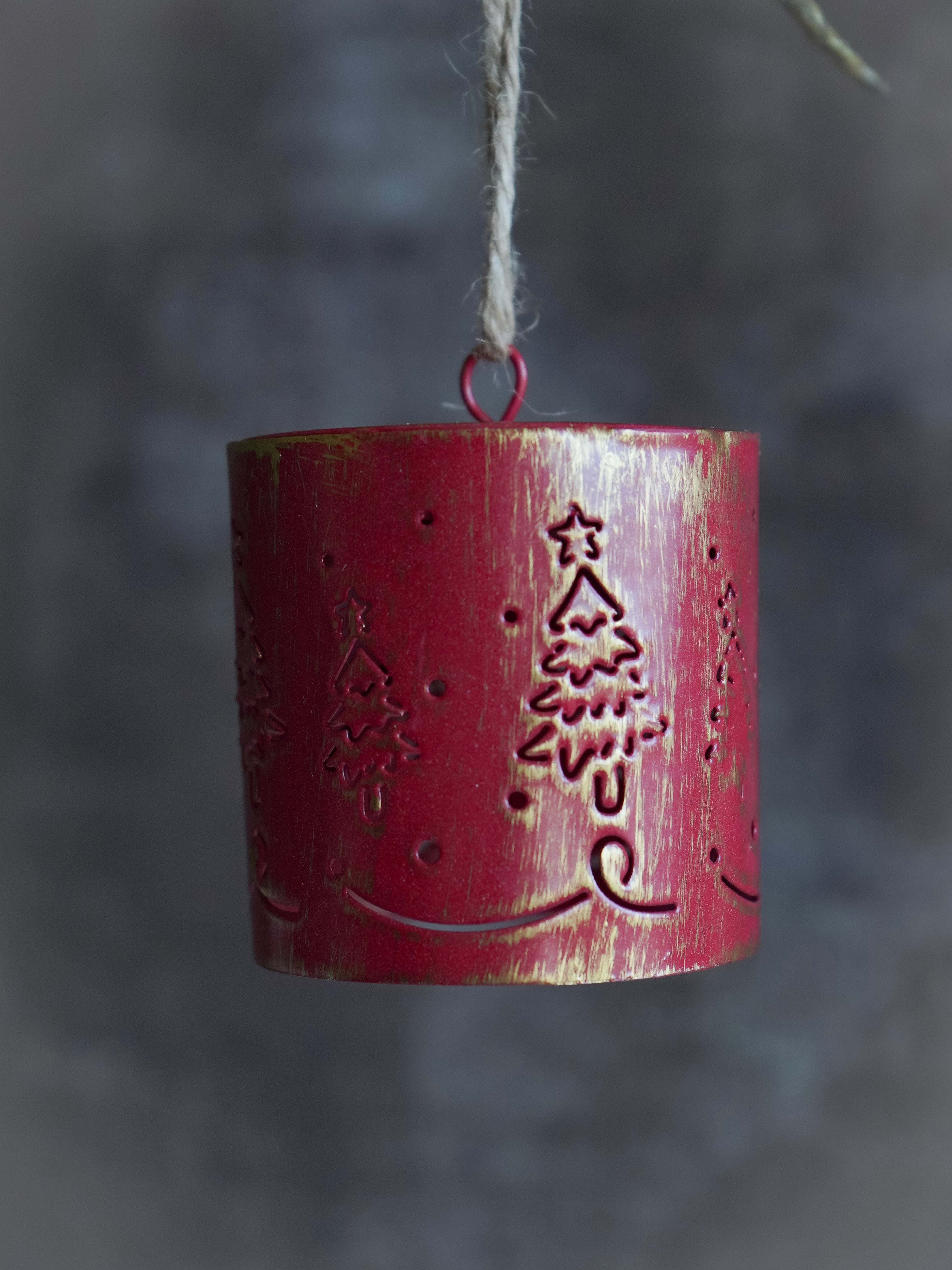 Red cylindrical hanging bell ornament with tree design on a dark background