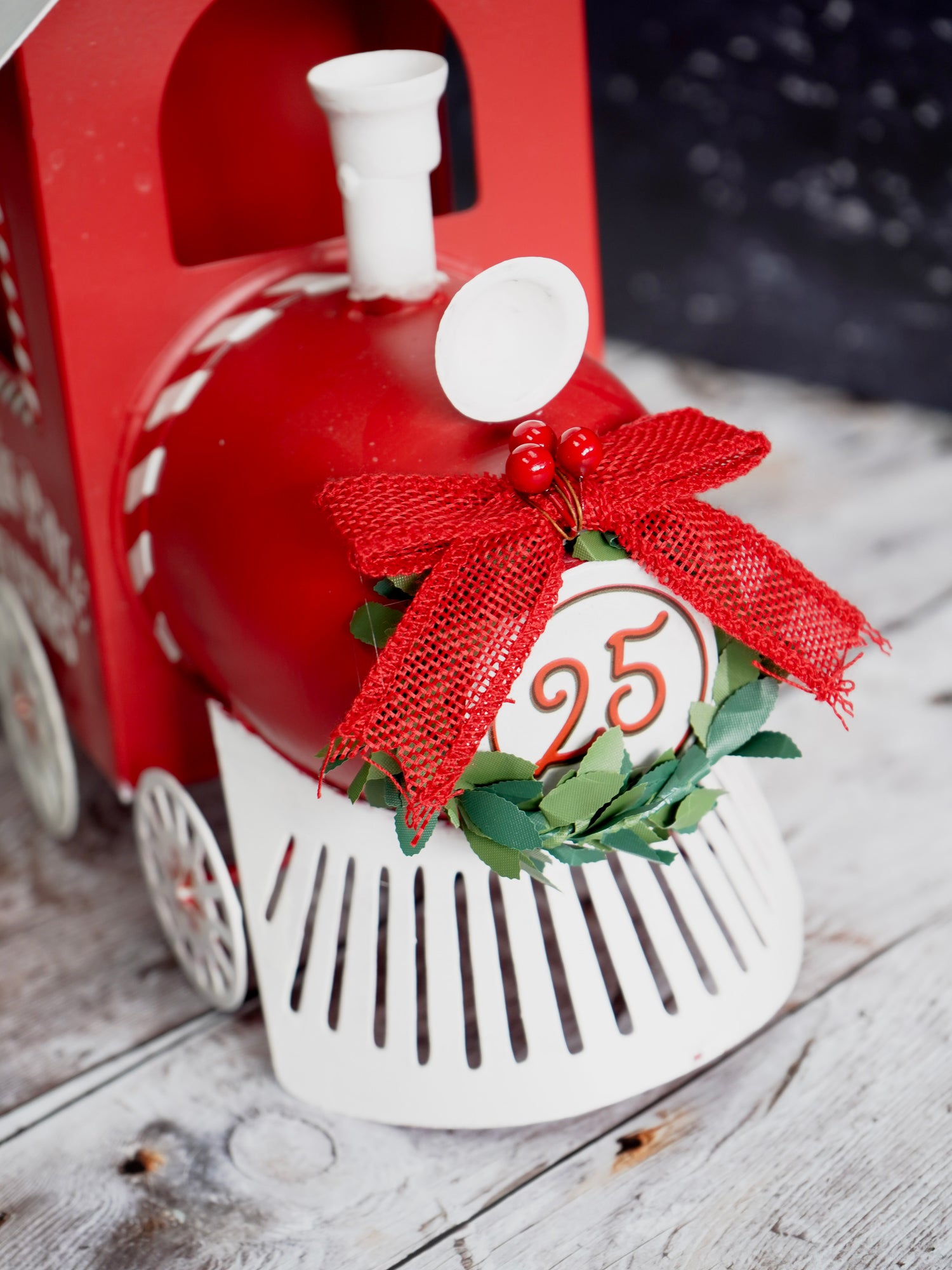 Red toy train with a decorative wreath and number 25 on a wooden surface
