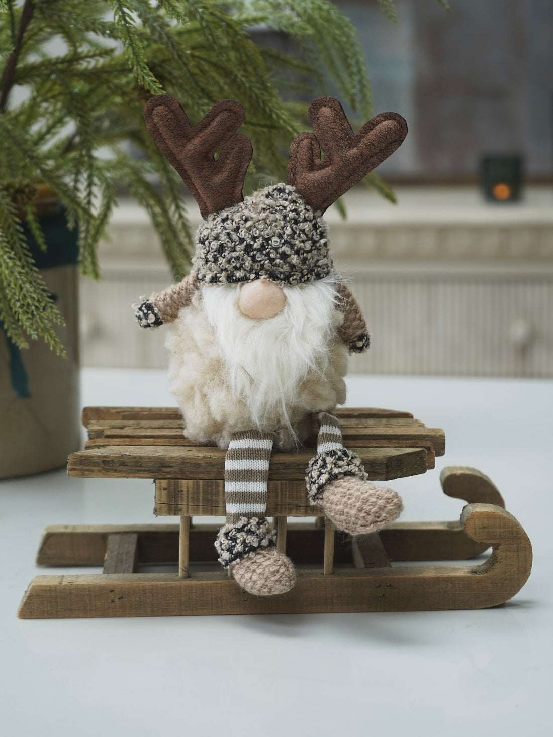 Gnome gonk with reindeer antlers sitting on a wooden sled in a decorative setting.