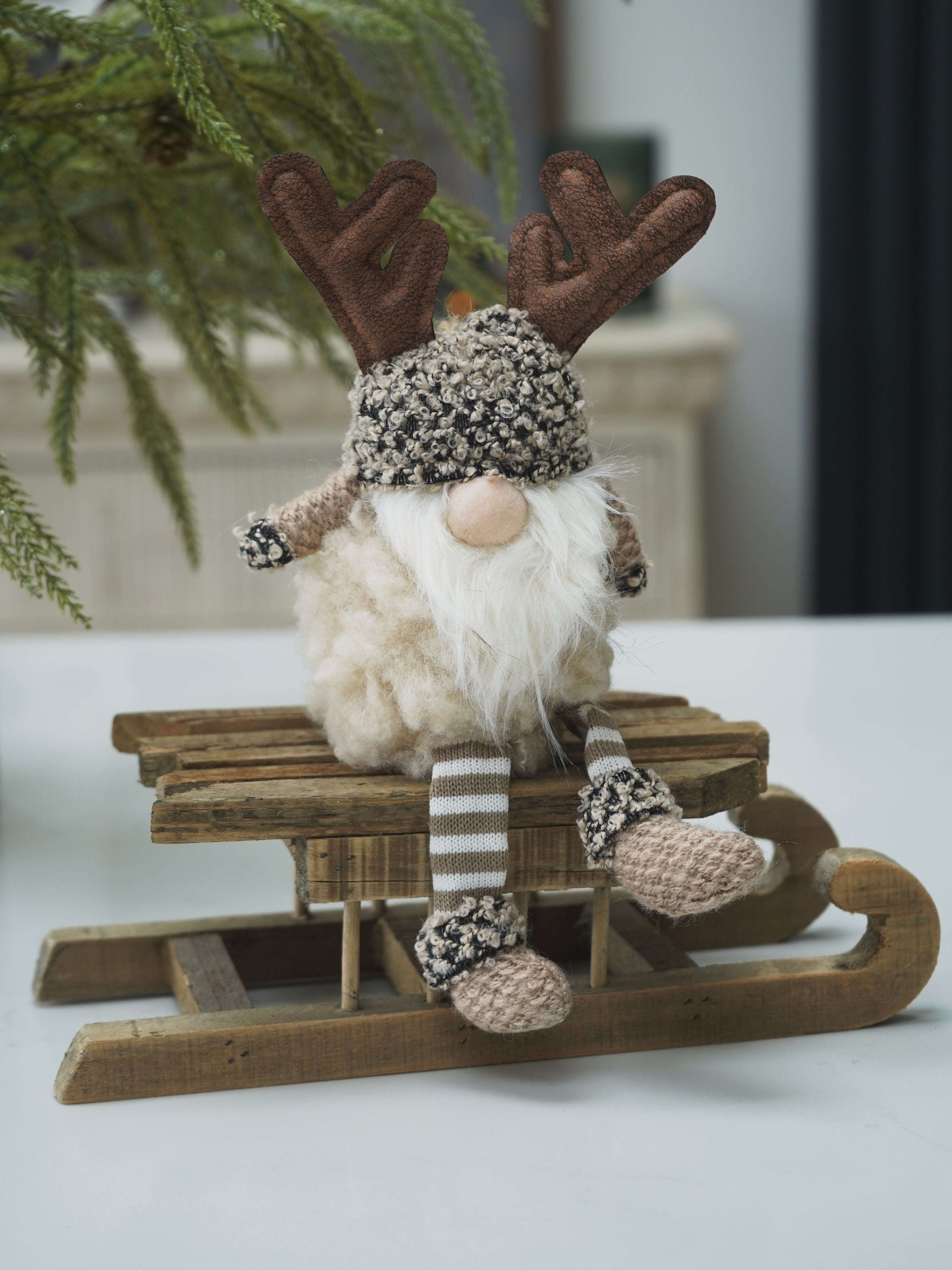 Decorative gnome gonk with reindeer antlers and a hat sitting on a small wooden sled.