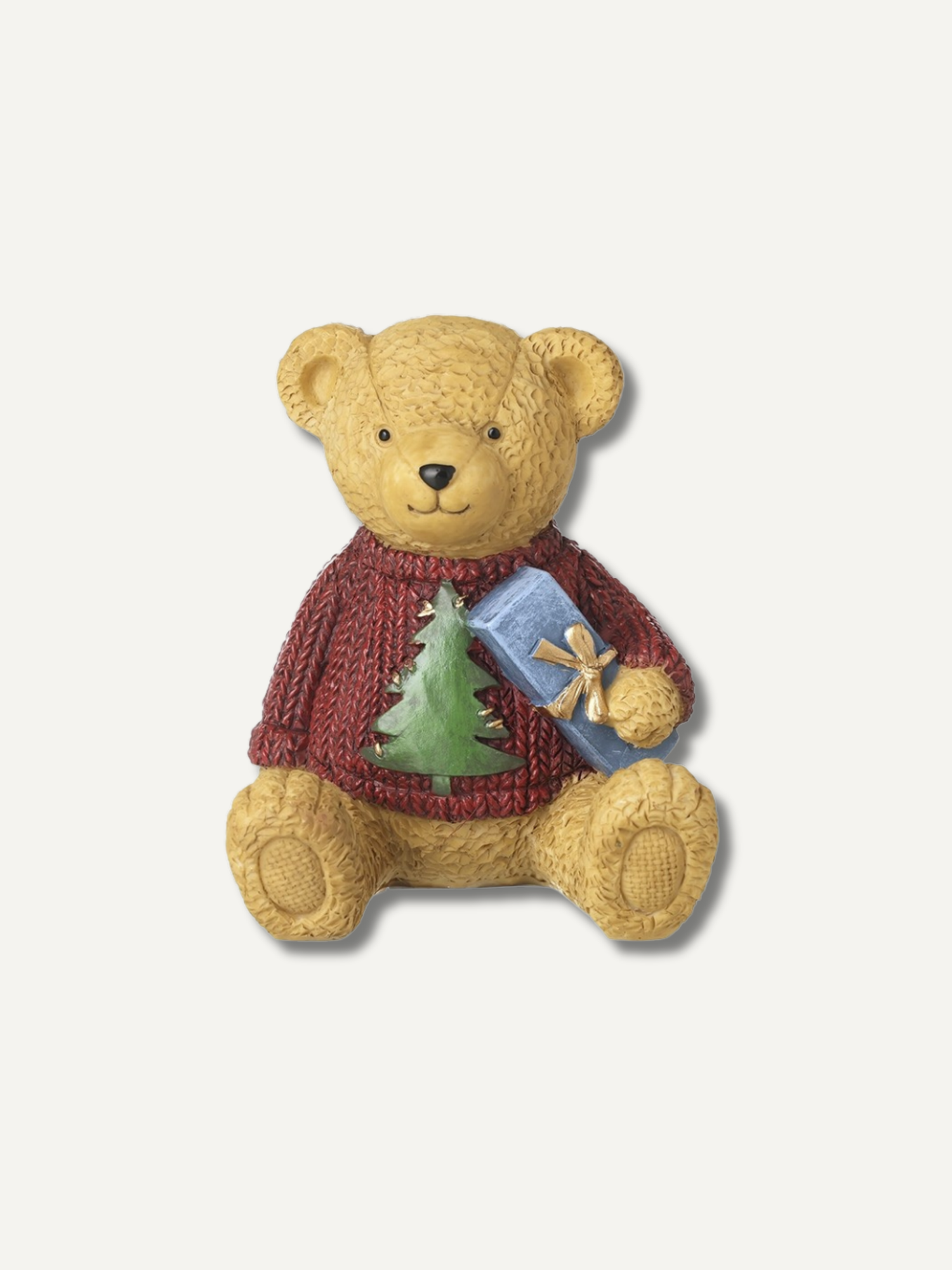 A teddy bear figurine wearing a red knit sweater with a green Christmas tree and holding a blue gift box, set against a plain light gray background.