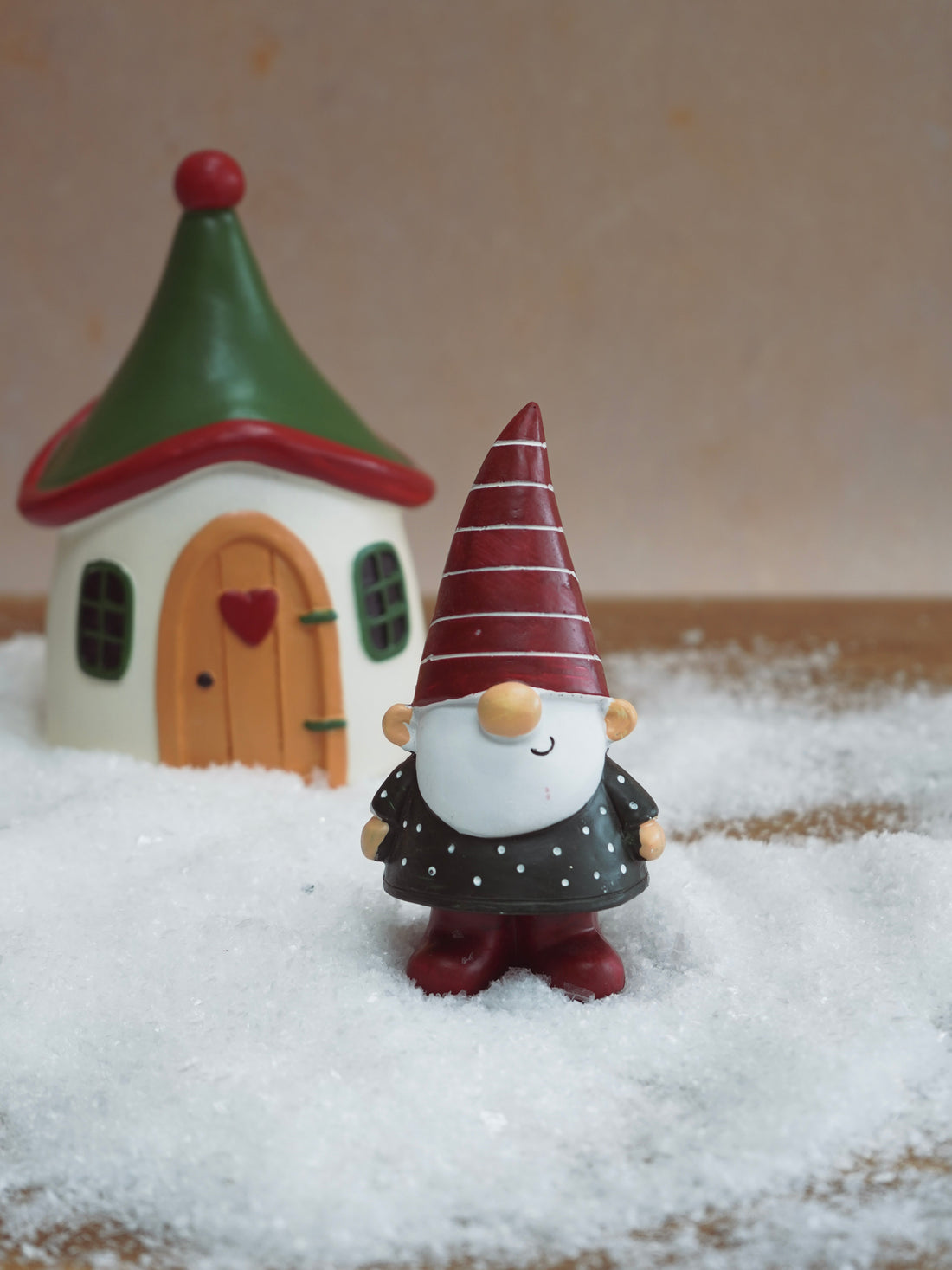 Decorative gnome figurine with a striped hat and small house in the background on a wooden surface.