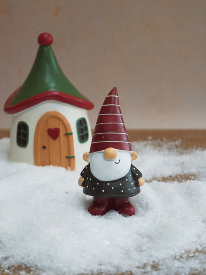 Decorative gnome figurine with a striped hat and small house in the background on a wooden surface.