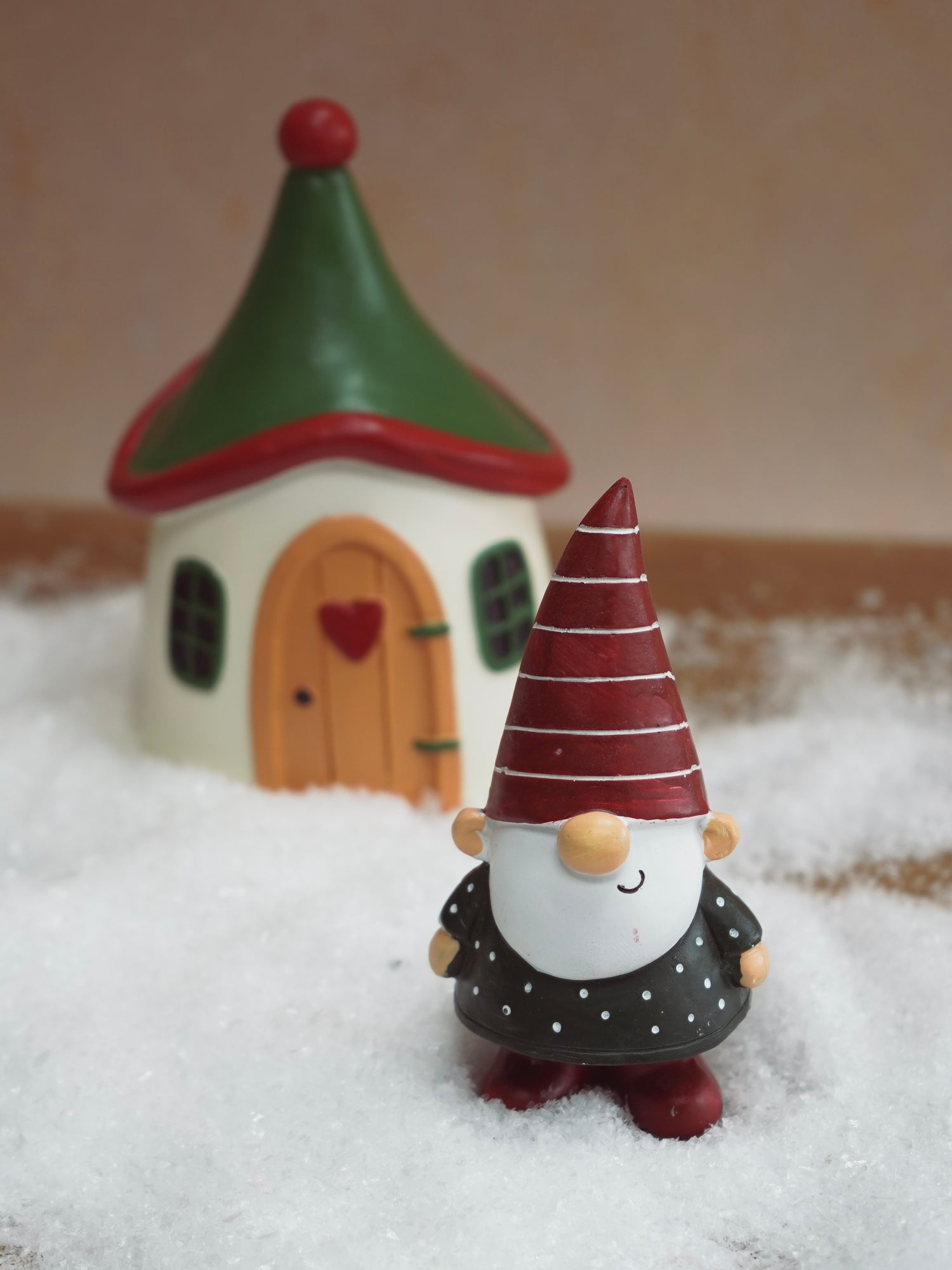 Gnome figurine with a red hat in front of a small house on a snowy background