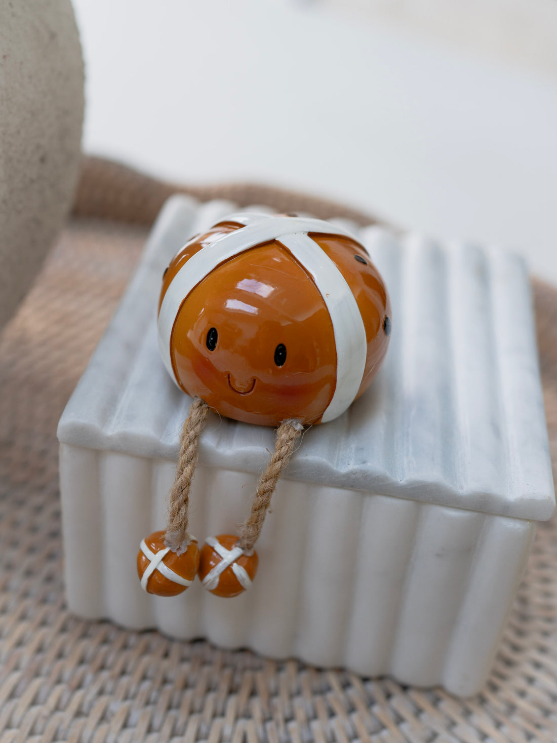 Small resin figurine of a easter hot cross bun ornament with a white cross on the top and dangly feet sat on ribbed marble box