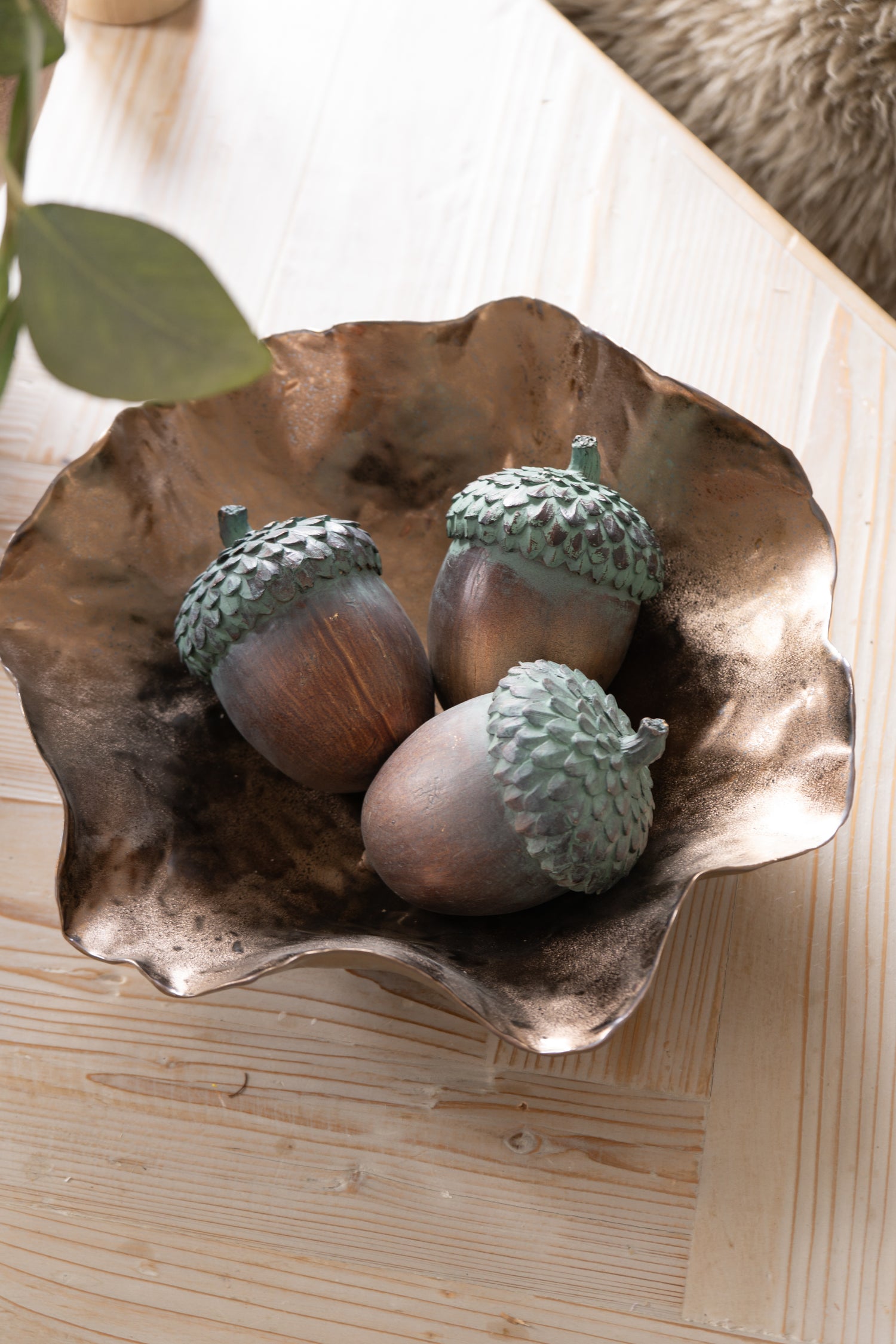 Decorative bronze bowl with acorn ornaments on a wooden surface