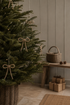 A decorated Christmas tree  with delicate bows in a wicker basket, styled in a cosy room with a wooden bench, wrapped gifts, and a basket against a paneled wall.