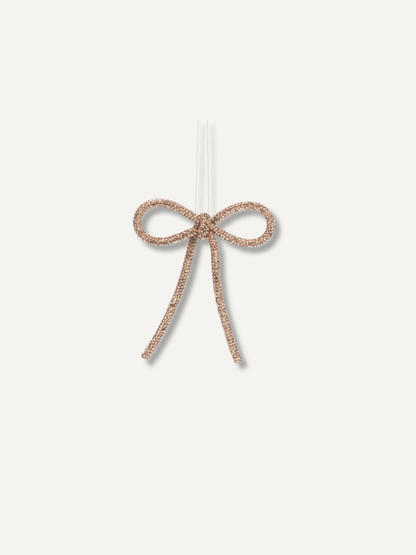 A small beaded bow ornament in a rose gold tone, suspended by a clear string against a plain off-white background.