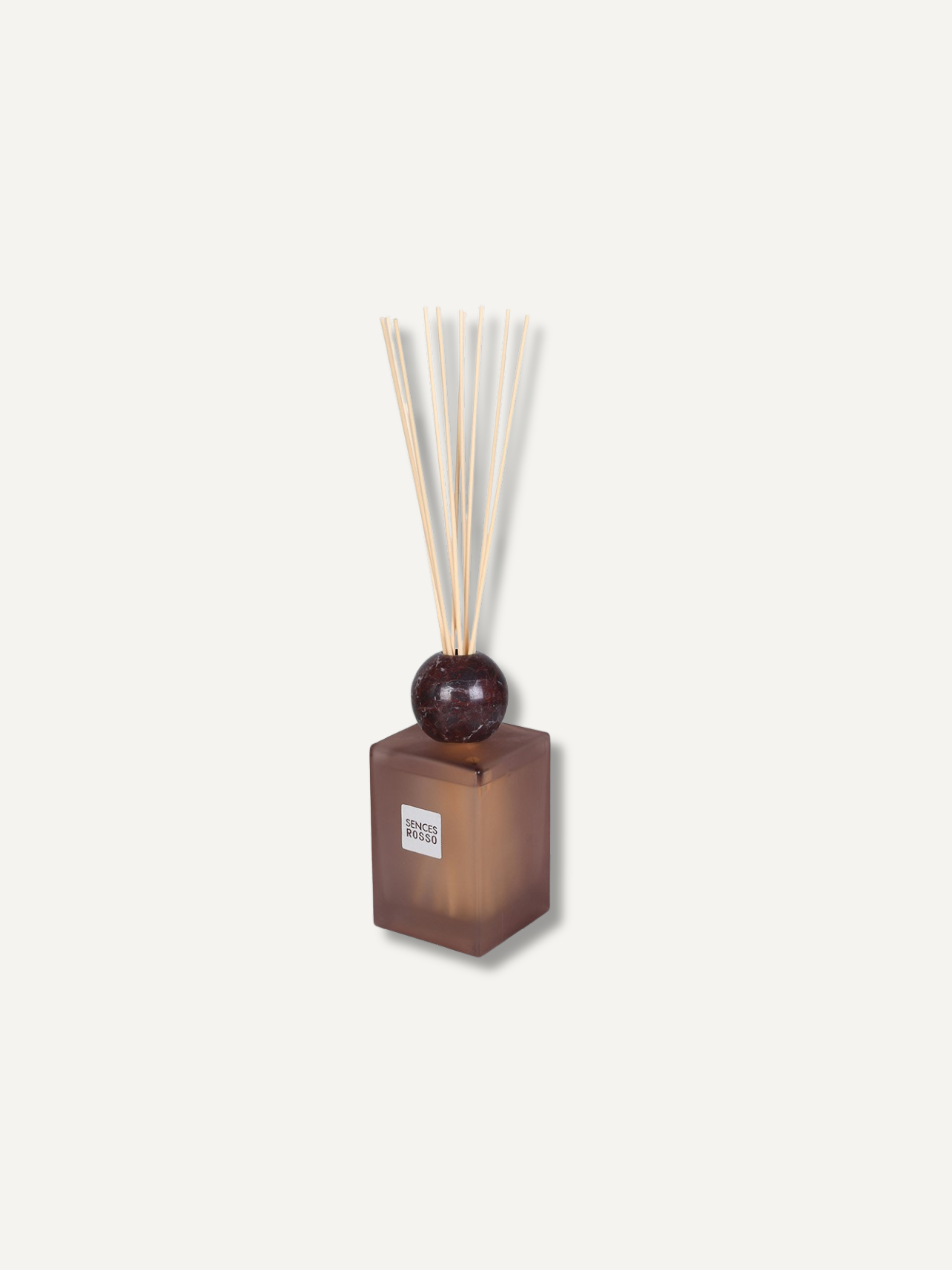 A reed diffuser with a translucent burgundy-brown rectangular glass bottle, a dark round stopper, and natural light wood reeds, shown on a plain off-white background.