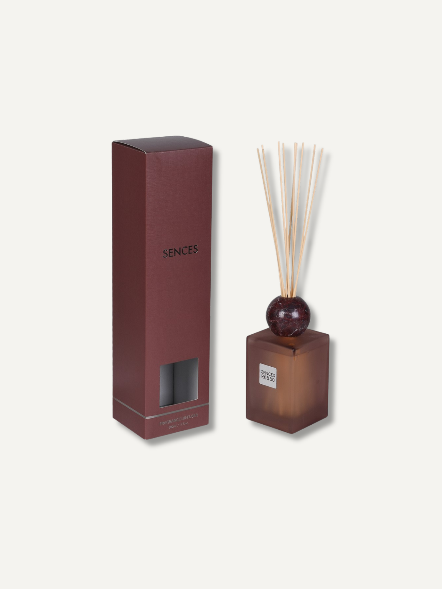 A reed diffuser set with a burgundy glass bottle, natural reeds, and a matching dark brown box, shown on a light beige background. The box is labeled &