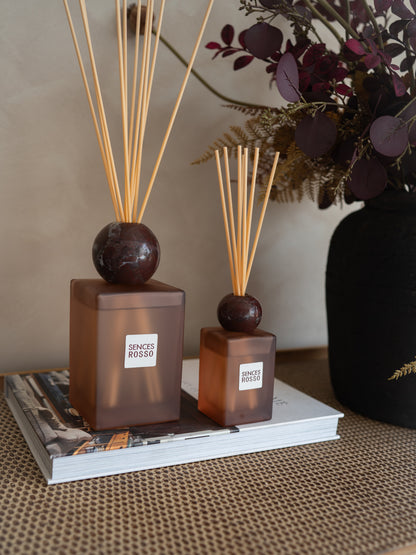 Two amber glass reed diffusers with dark round tops and natural reeds, labeled &