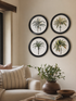 Four circular wall art pieces with palm tree designs on a beige wall above a sofa.