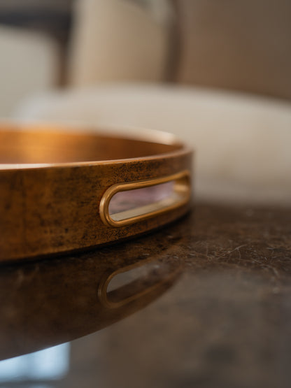 A close-up of a round gold edged tray cut out handle resting on a dark reflective surface.