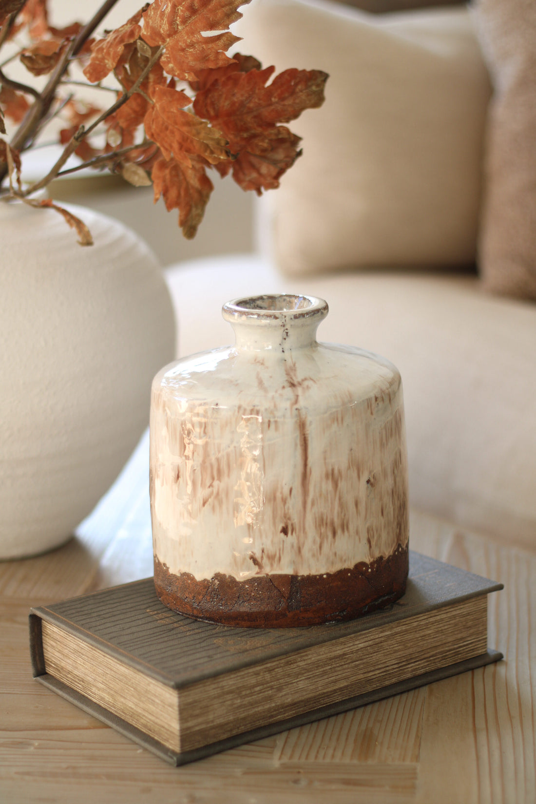 Terracotta vase on a book with autumn leaves and a beige sofa in the background
