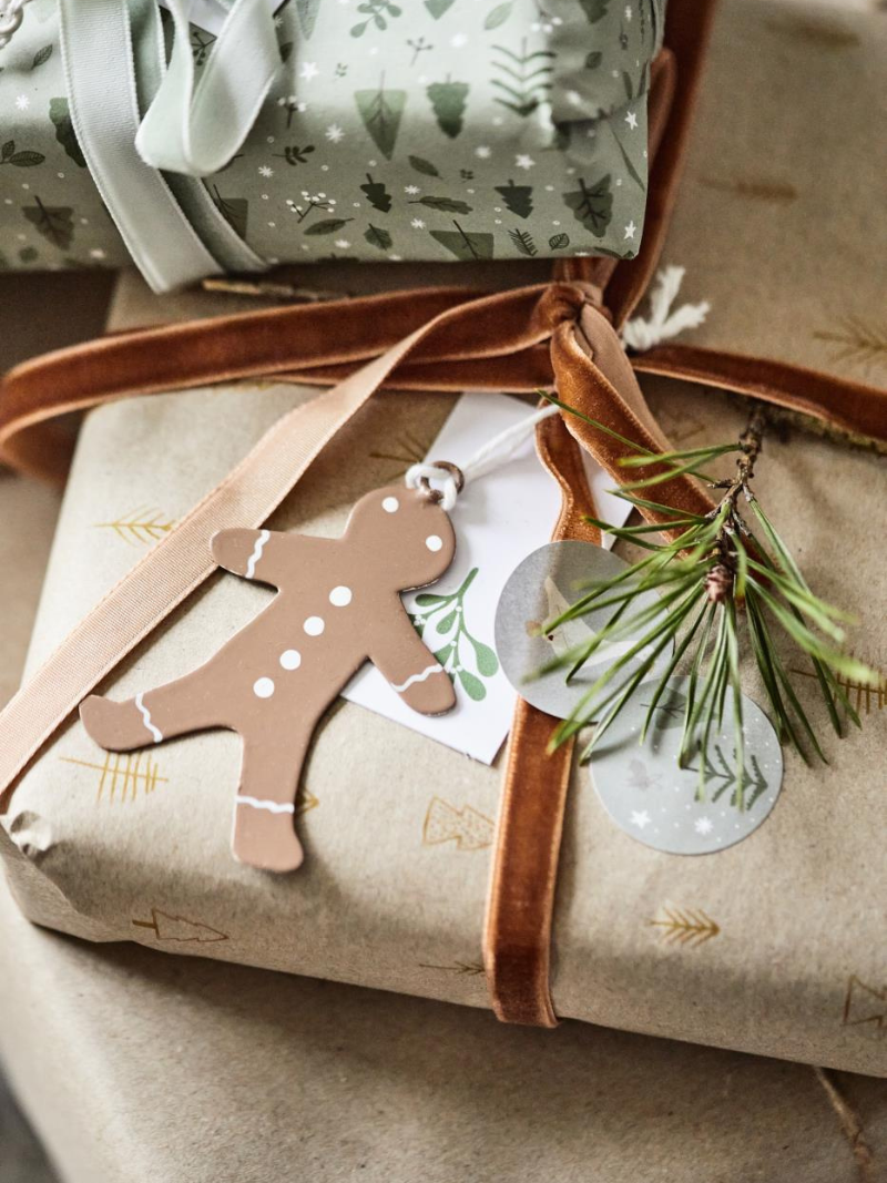 Gift wrapped in brown paper with a gingerbread man tag and greenery, on a neutral background.