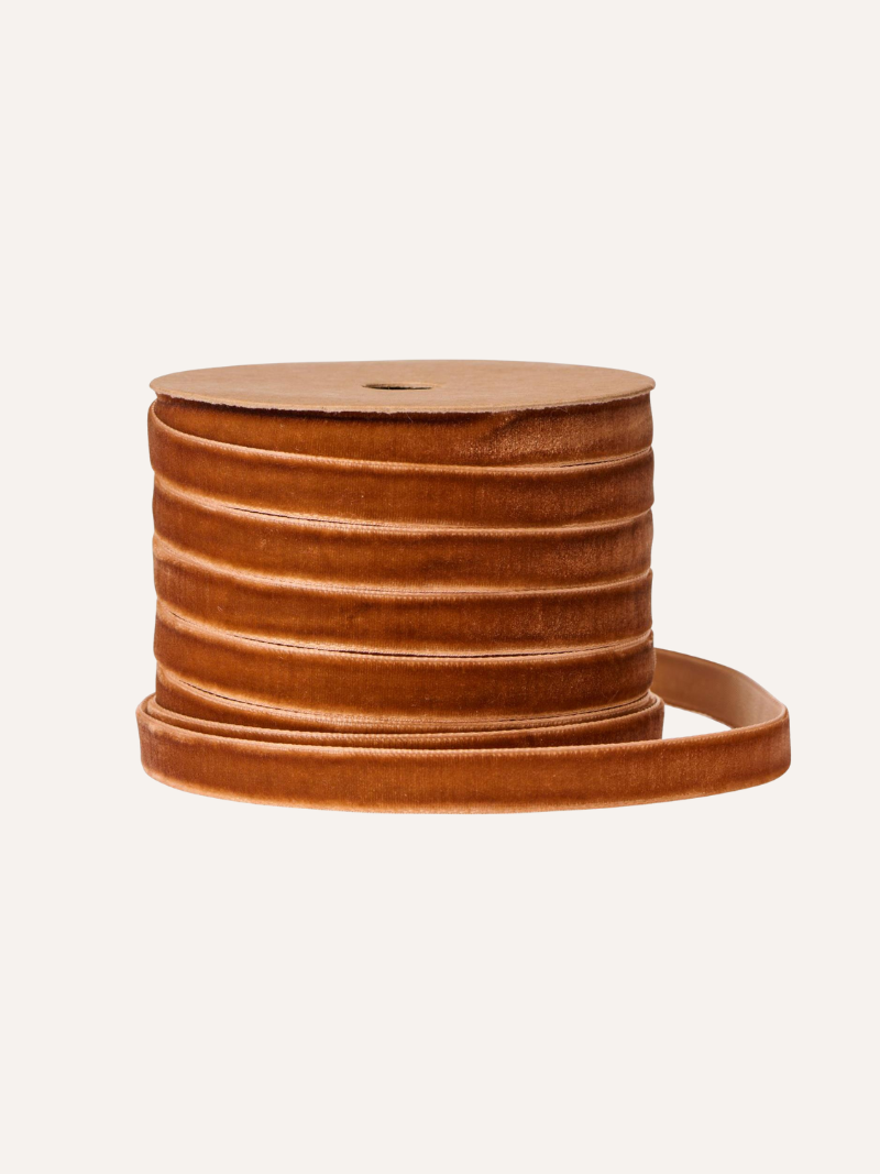Spool of rust velvet ribbon on a beige background
