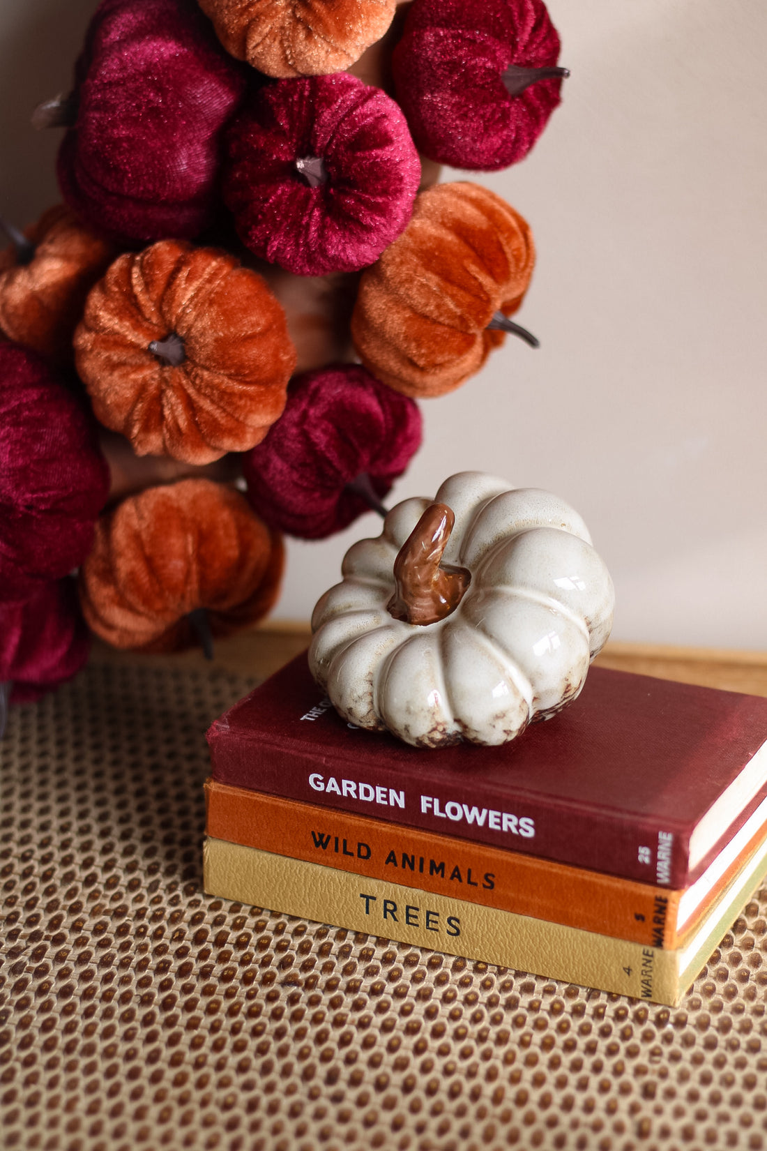 Decorative white pumpkin on books with a colorful pumpkin wreath in the background