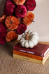 Decorative white pumpkin on books with a colorful pumpkin wreath in the background
