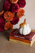 Decorative white pumpkin with orange stem on top of books with a pumpkin-themed wreath in the background.