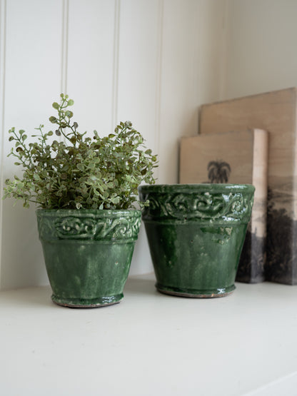 Two green ceramic pots with plants on a white surface