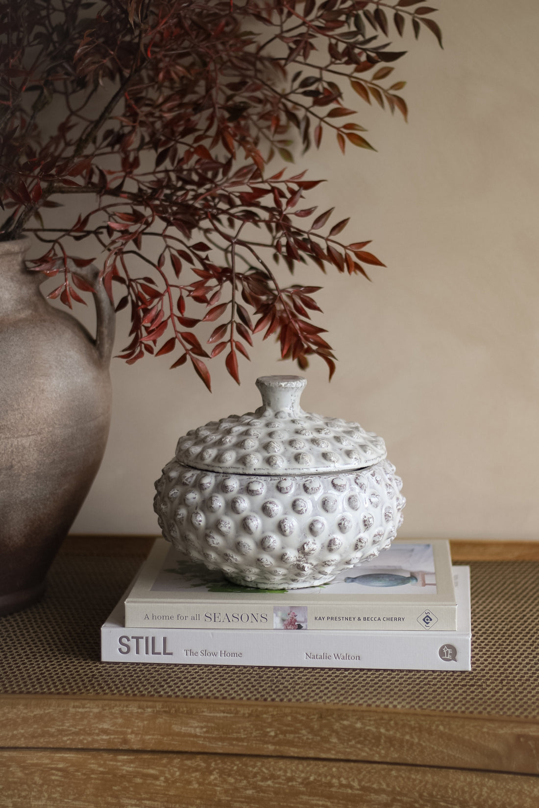 White textured ceramic lid on books with a vase and branches in the background