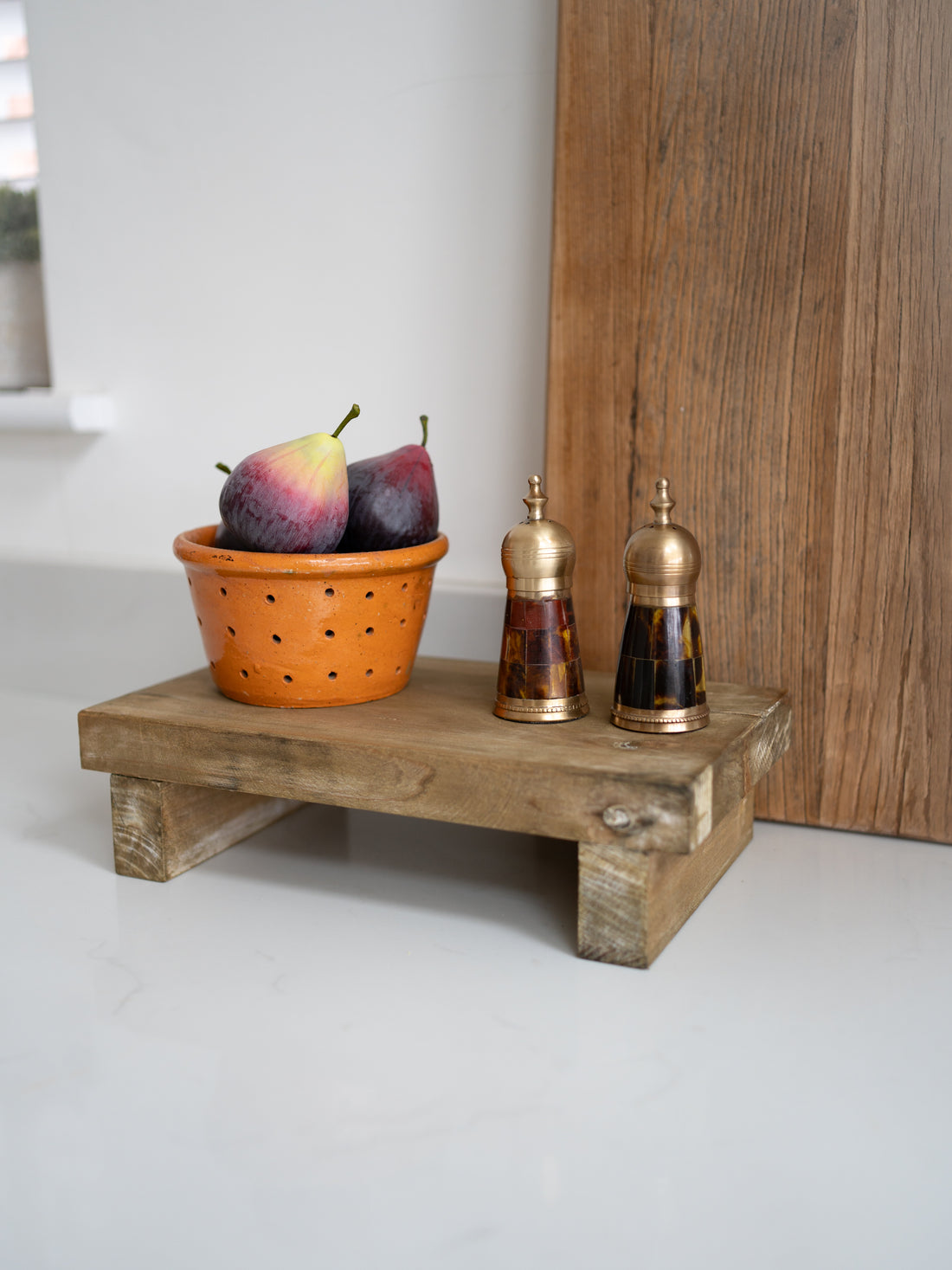 Wooden tray with fruits, a colander, and salt and pepper shakers on a white surface.