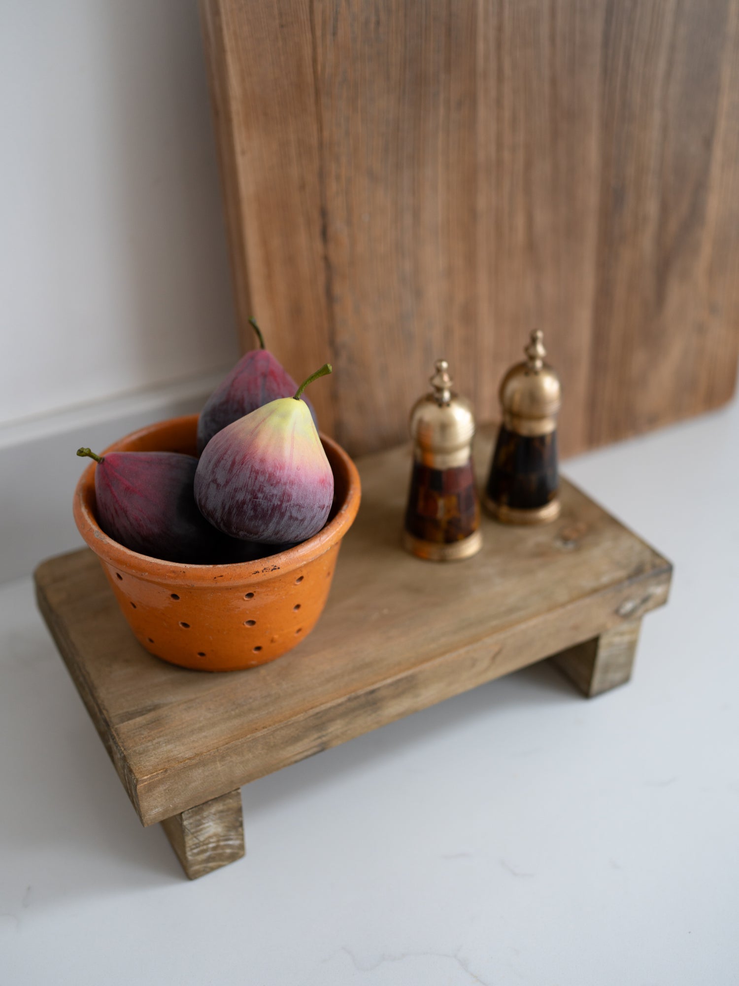 Figs in a terracotta pot on a wooden stand with a wooden board in the background.