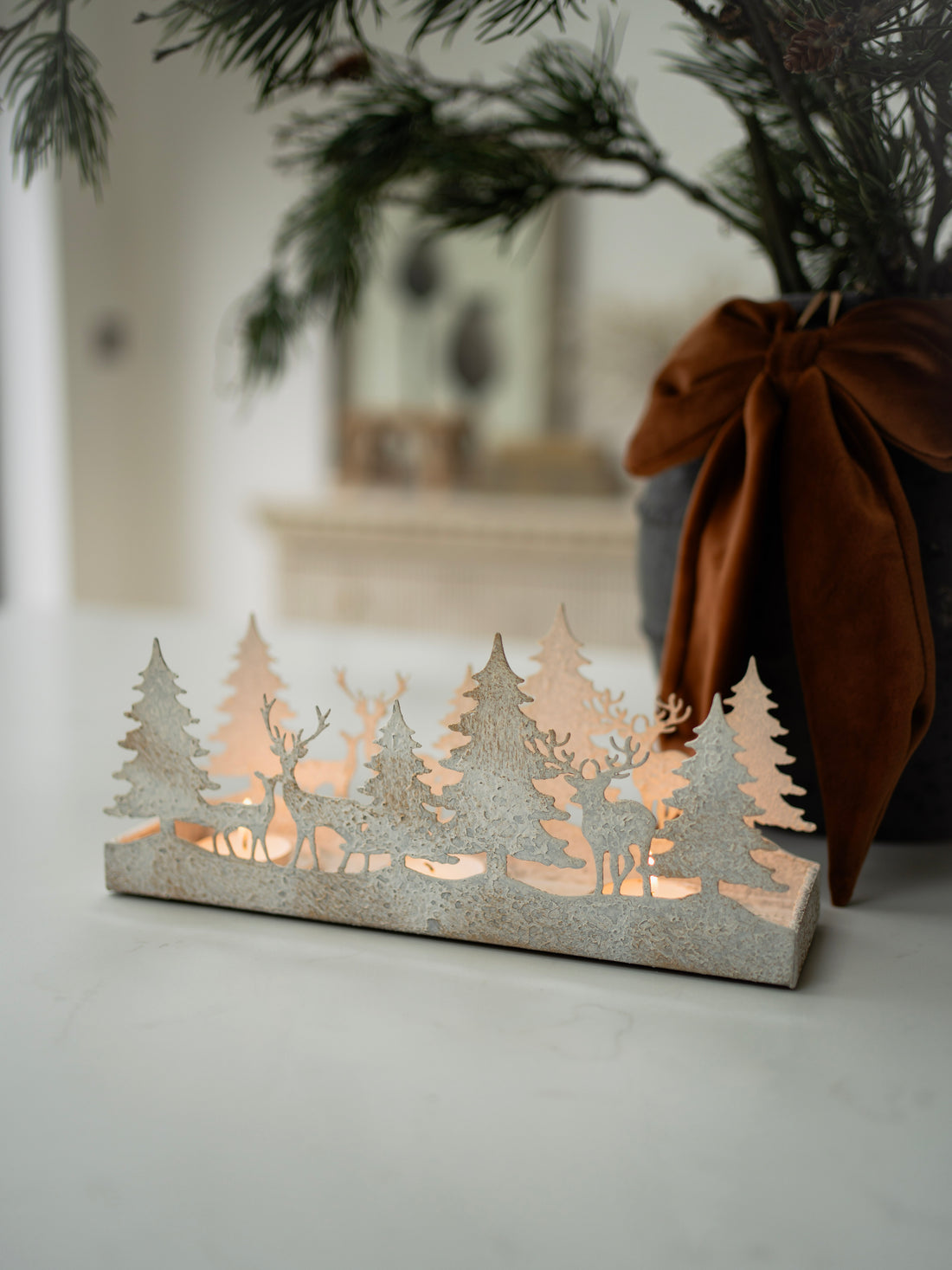 Decorative lantern with cut-out design of trees and deer on a neutral background