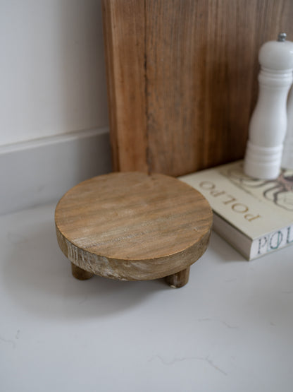 Small wooden stool on a white floor with a book and white pepper grinder in the background.