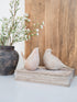 Decorative stone birds on a wooden block with a vase of flowers in the background.