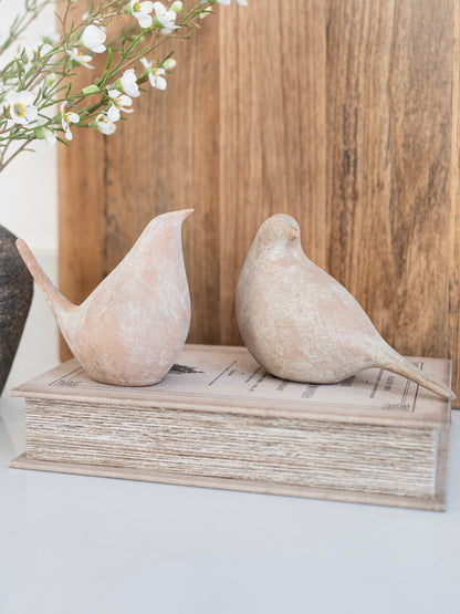 Two stone birds on a stack of books with a wooden panel and flowers in the background