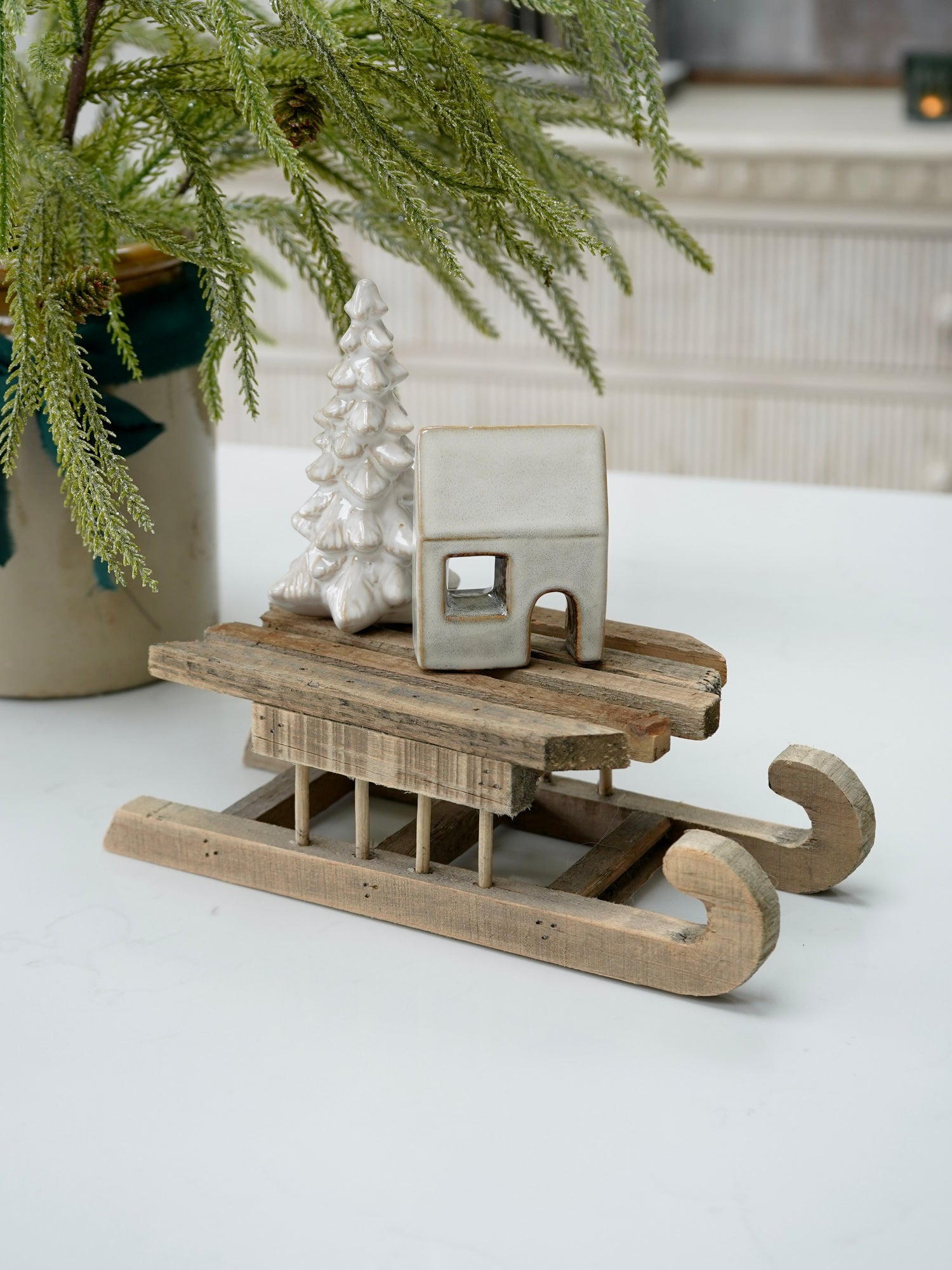 Wooden sled with a small house on top next to a plant indoors