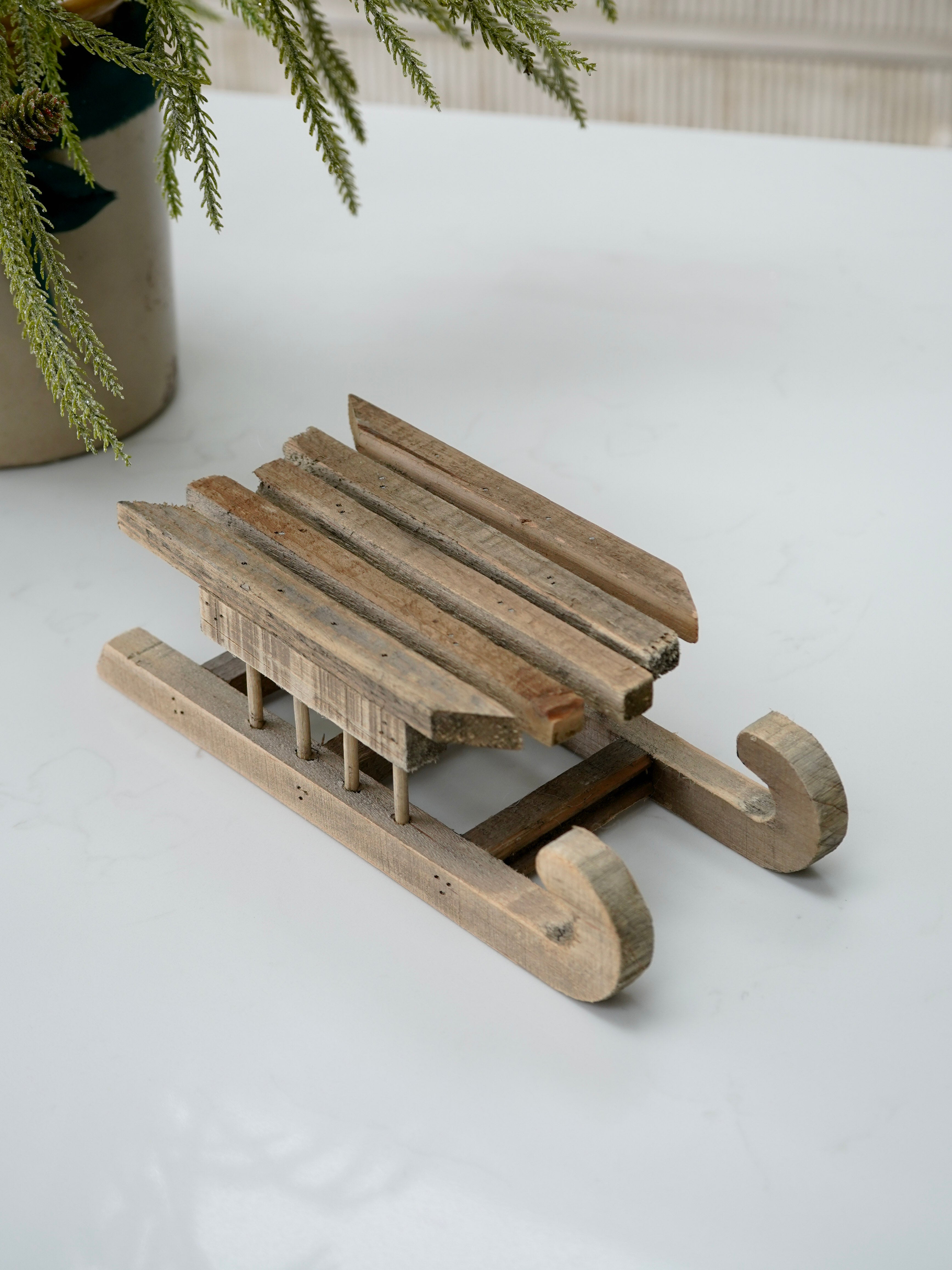 Wooden sled on a white surface with a plant in the background