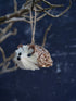 Decorative hedgehog ornament hanging from a branch against a dark background