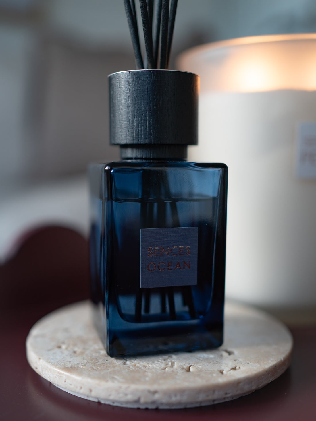A reed diffuser bottle with a dark blue glass body and black reeds, labeled &