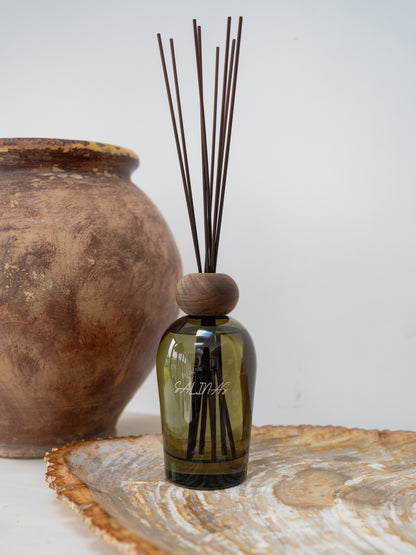 A green diffuser bottle with wooden cap and sticks on a decorative surface.