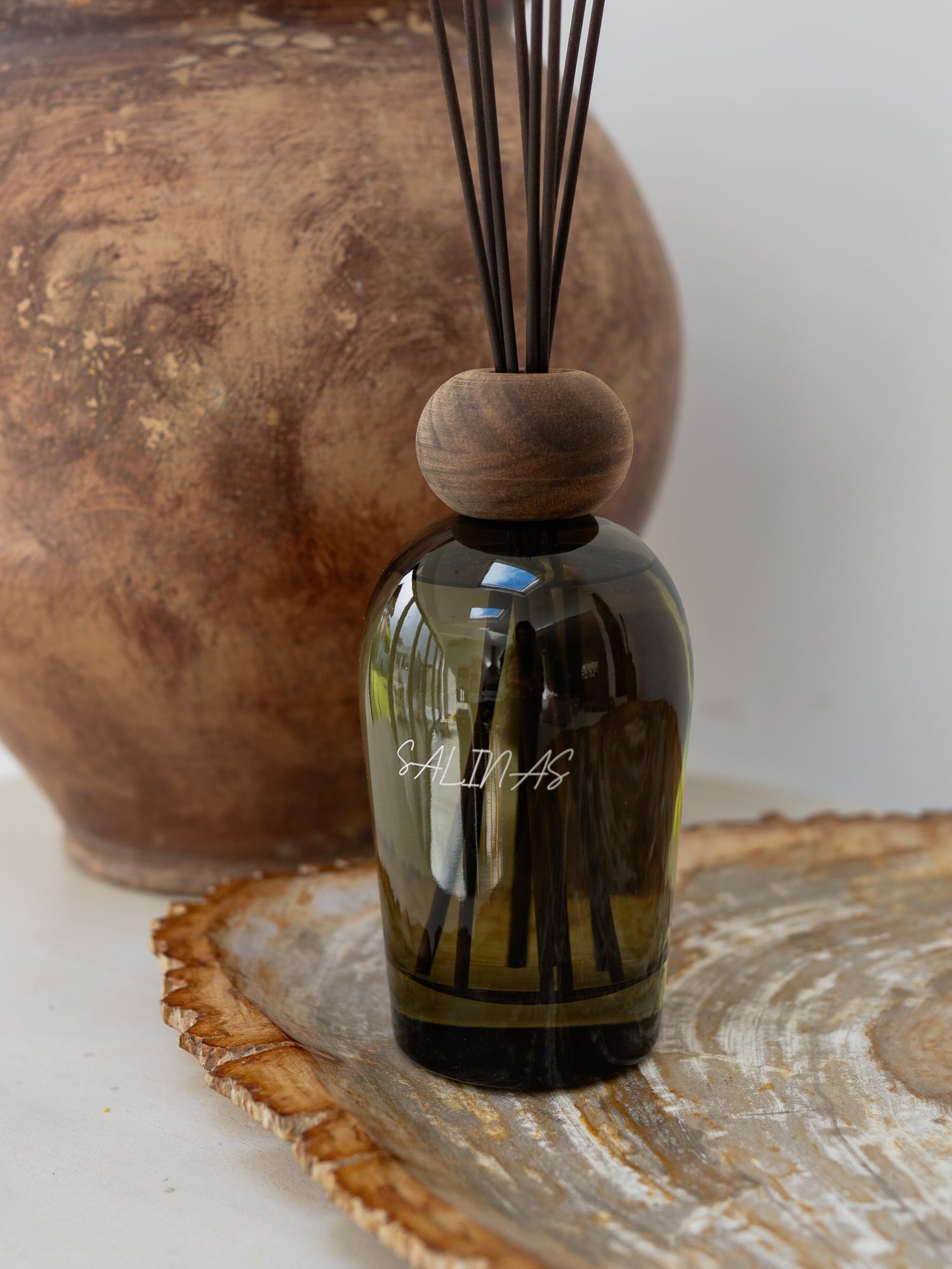 A green salinas diffuser bottle with dark wooden top on a decorative surface